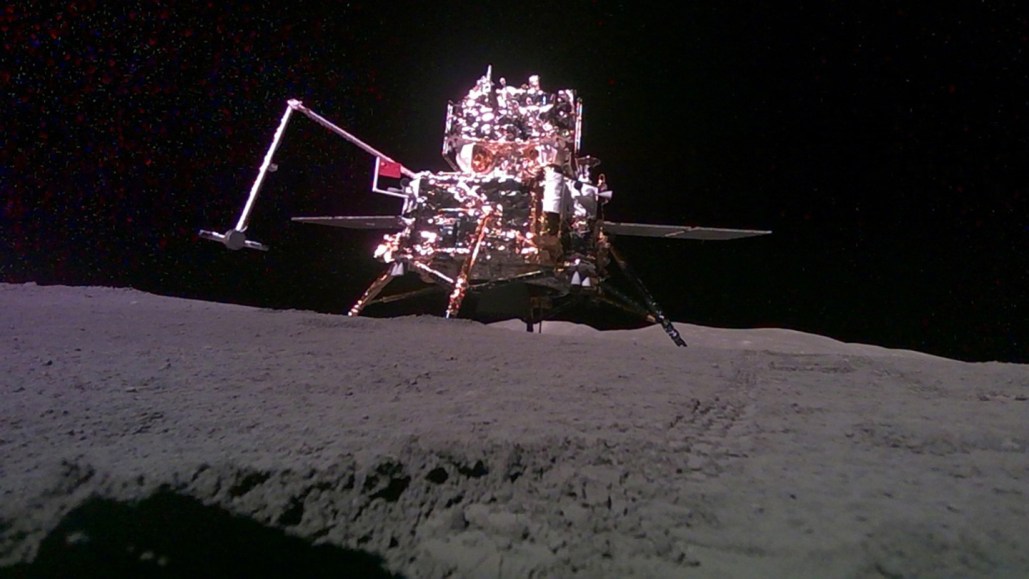 A shiny robotic lunar lander sits on a gray surface with a black background.